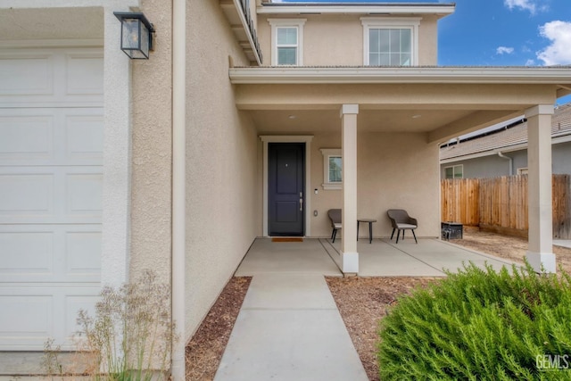 doorway to property with a garage, stucco siding, and fence