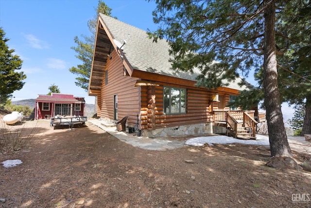 rear view of property featuring an outdoor structure, log exterior, and a shingled roof