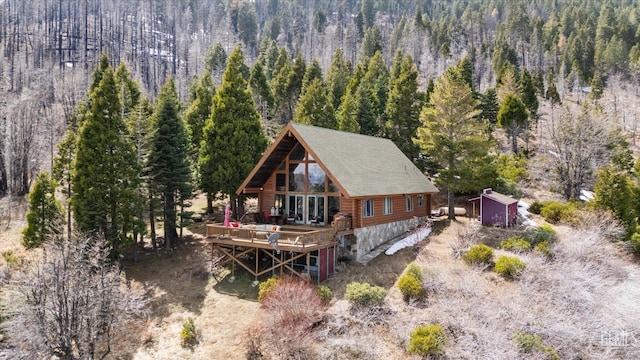 back of property featuring a forest view, a wooden deck, and log siding