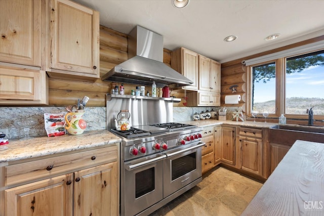 kitchen with rustic walls, wall chimney range hood, range with two ovens, a sink, and light brown cabinetry