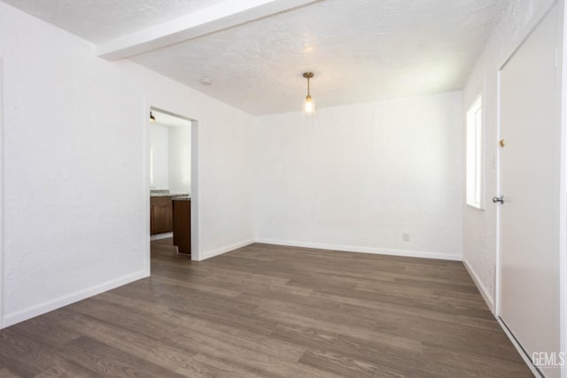 empty room featuring a textured ceiling, dark hardwood / wood-style floors, and beamed ceiling