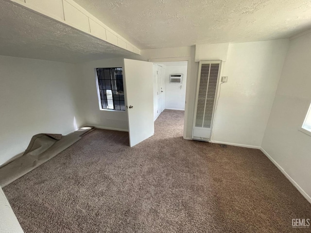 unfurnished room featuring a wall mounted air conditioner, dark carpet, and a textured ceiling