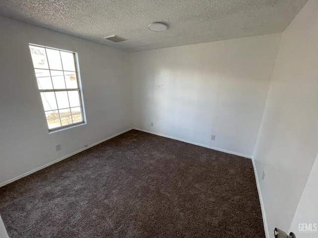 spare room featuring dark colored carpet and a textured ceiling