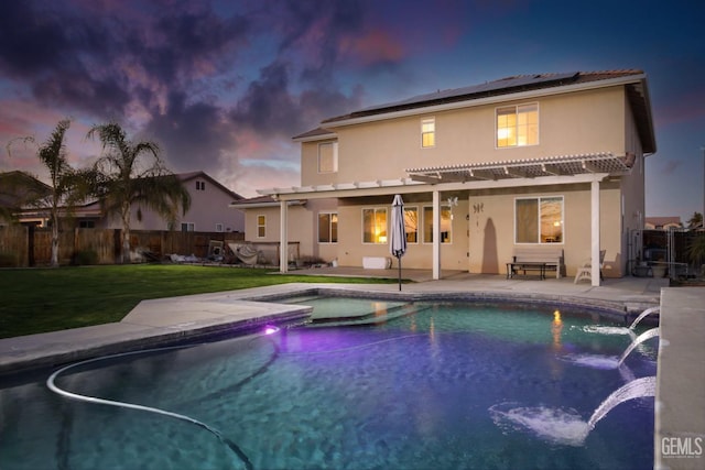 back house at dusk featuring a lawn, pool water feature, solar panels, a pergola, and a patio