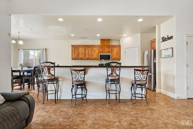 605 Cornelia St, Wasco, CA 93280 - kitchen with freestanding refrigerator, recessed lighting, a breakfast bar, dark countertops, and brown cabinetry