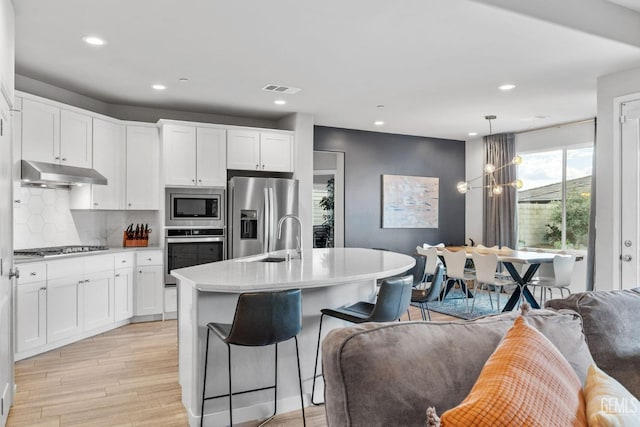 kitchen featuring visible vents, light wood-style flooring, light countertops, under cabinet range hood, and appliances with stainless steel finishes