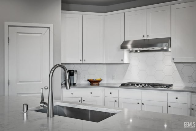 kitchen with under cabinet range hood, stainless steel gas cooktop, white cabinets, and a sink