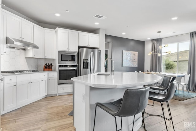 kitchen with visible vents, backsplash, under cabinet range hood, stainless steel appliances, and a sink