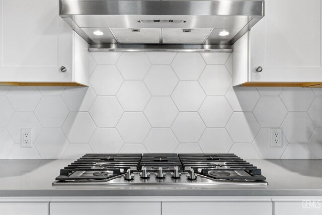 room details with decorative backsplash, stainless steel gas stovetop, wall chimney exhaust hood, and white cabinets