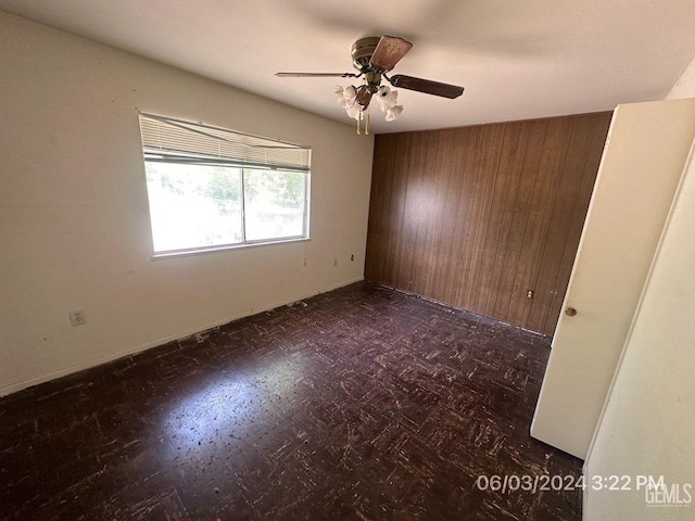 unfurnished room with ceiling fan and wood walls