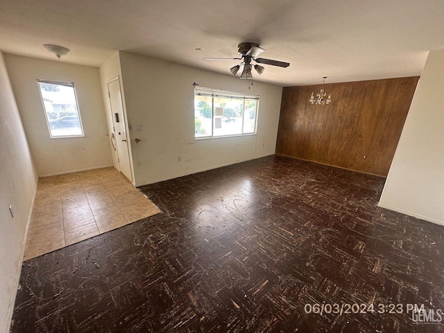 interior space with ceiling fan with notable chandelier, plenty of natural light, and wood walls