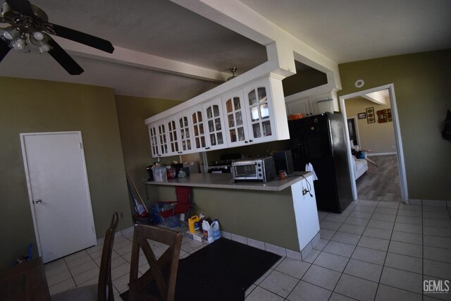 kitchen featuring kitchen peninsula, black refrigerator, ceiling fan, white cabinetry, and light tile patterned flooring