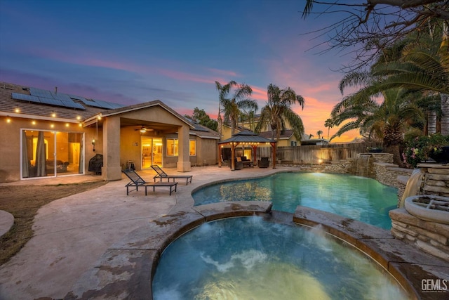 pool at dusk featuring a gazebo, pool water feature, an in ground hot tub, and a patio area