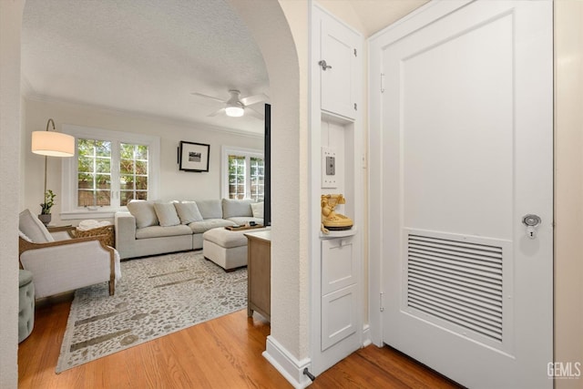 living area with ornamental molding, a ceiling fan, a textured ceiling, wood finished floors, and arched walkways