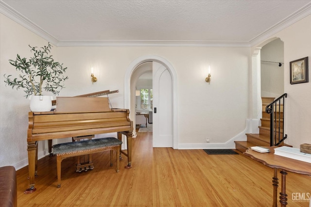 living area featuring wood finished floors, arched walkways, stairs, a textured ceiling, and crown molding