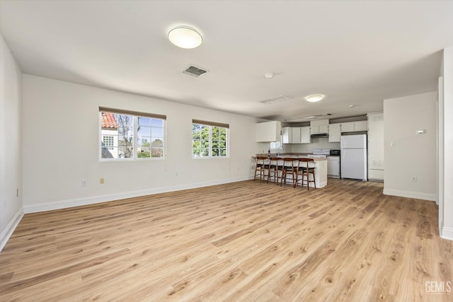 unfurnished living room featuring light wood finished floors, visible vents, and baseboards