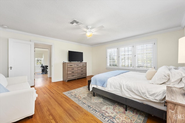 bedroom featuring a ceiling fan, visible vents, light wood finished floors, baseboards, and crown molding