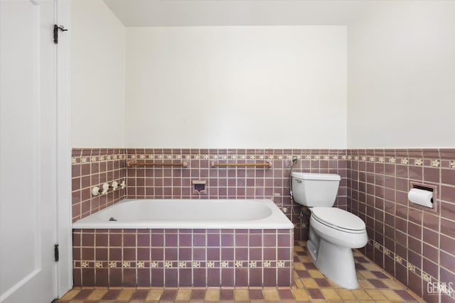 full bath featuring a wainscoted wall, toilet, tile walls, and a bath