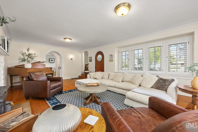 living room with wood finished floors, arched walkways, stairs, a textured ceiling, and crown molding