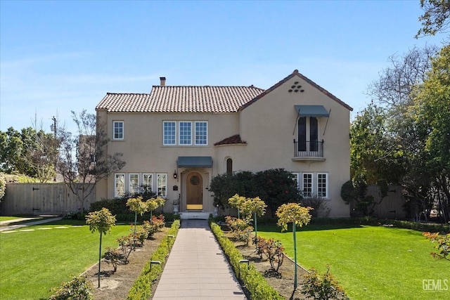 mediterranean / spanish-style home with stucco siding, a tile roof, a front lawn, and fence