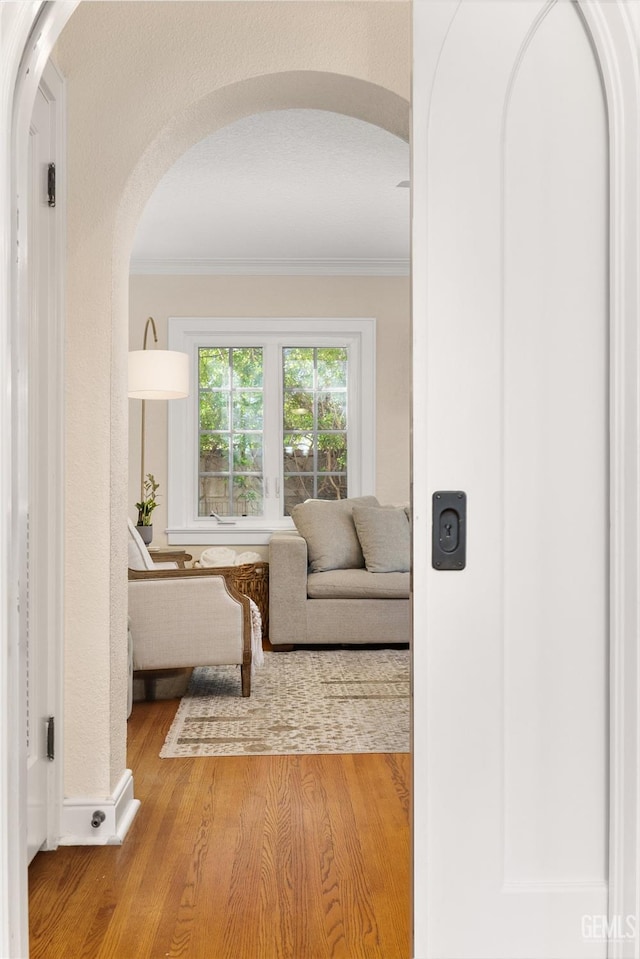 hallway with arched walkways, ornamental molding, and wood finished floors