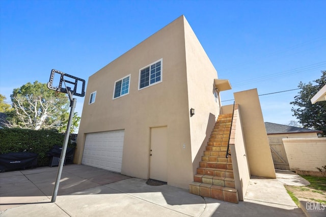 exterior space featuring fence, stairs, stucco siding, a garage, and driveway