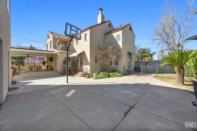 rear view of house featuring a gate, fence, a chimney, stucco siding, and a tile roof