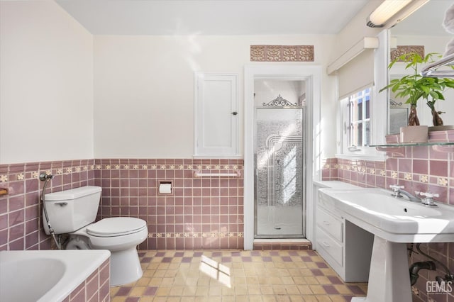 bathroom with a wainscoted wall, a stall shower, tiled bath, tile walls, and toilet