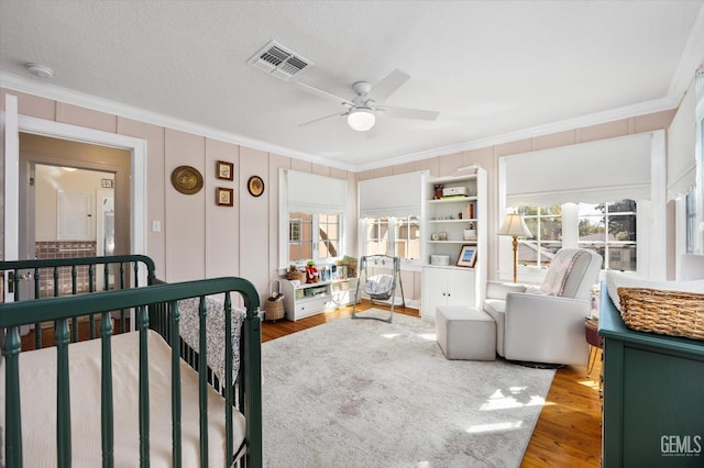 bedroom featuring crown molding, wood finished floors, visible vents, and a textured ceiling