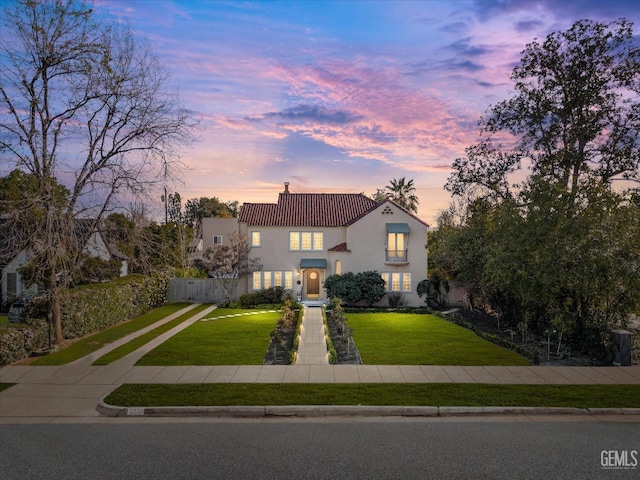 mediterranean / spanish-style home with a front yard, fence, a chimney, stucco siding, and a tiled roof