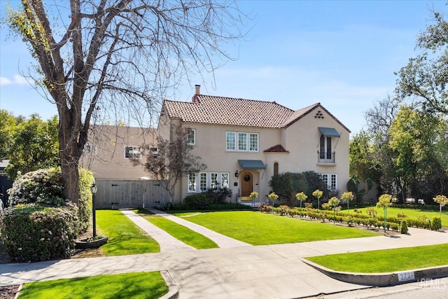 mediterranean / spanish-style home featuring a front lawn, fence, a tile roof, stucco siding, and a chimney