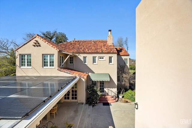 rear view of house with stucco siding, a chimney, and a tile roof