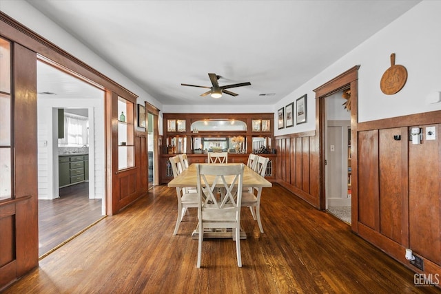 dining room featuring wainscoting, dark wood finished floors, and ceiling fan