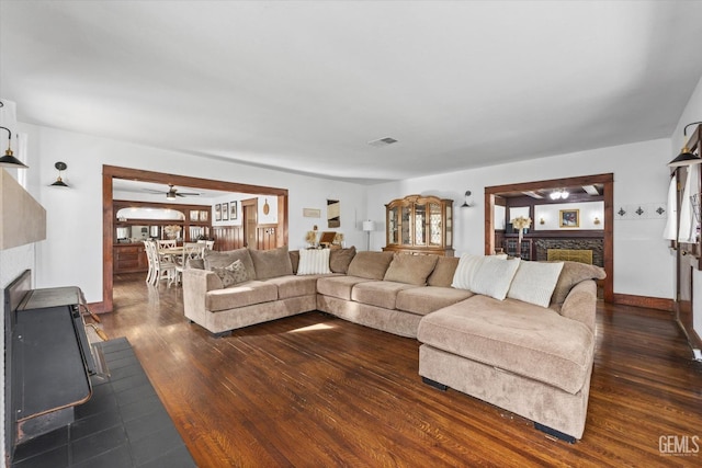 living area with dark wood-style floors, visible vents, a stone fireplace, and baseboards