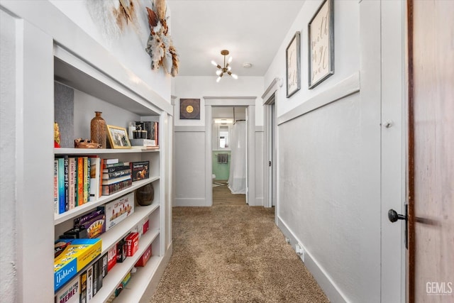 hallway with carpet floors, baseboards, and a notable chandelier