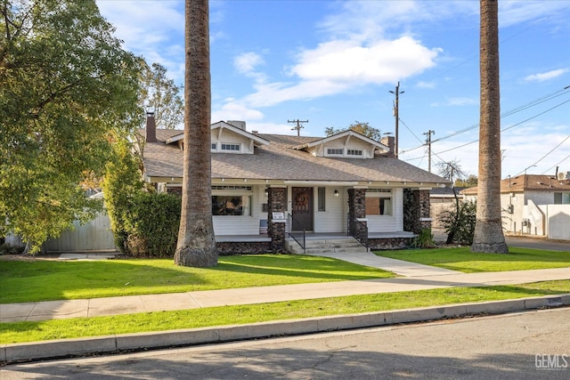 craftsman inspired home with a porch, a shingled roof, a chimney, and a front yard