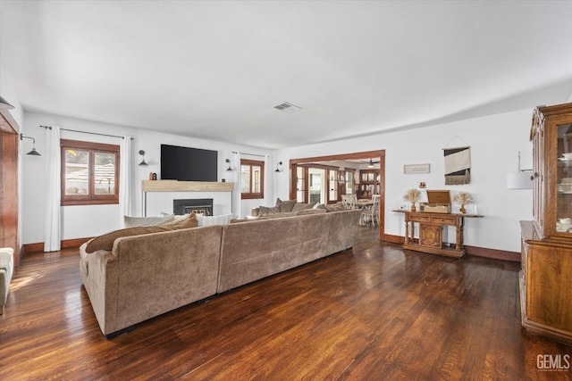 living area featuring dark wood-style flooring, visible vents, a fireplace, and baseboards