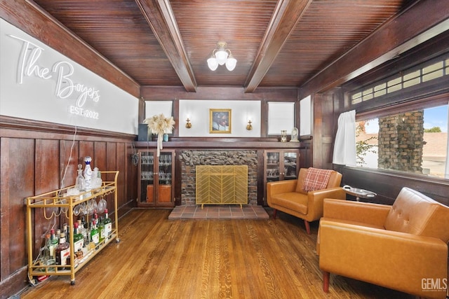 living area featuring beam ceiling, a fireplace, wainscoting, wood finished floors, and wooden ceiling