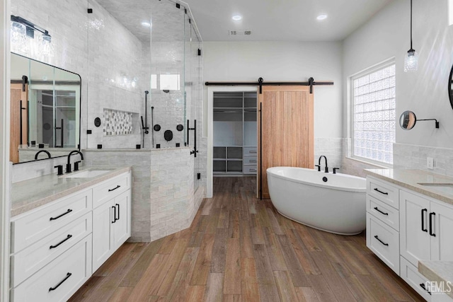 full bathroom featuring a shower stall, a sink, two vanities, tile walls, and wood finished floors