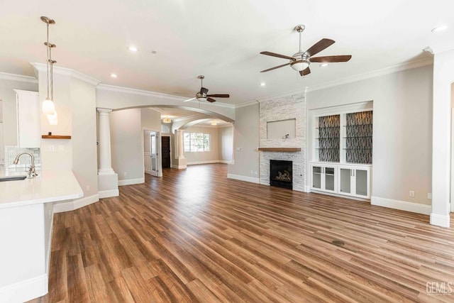 unfurnished living room featuring a sink, ceiling fan, arched walkways, ornamental molding, and wood finished floors