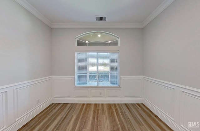 empty room with visible vents, wainscoting, light wood-style floors, and crown molding