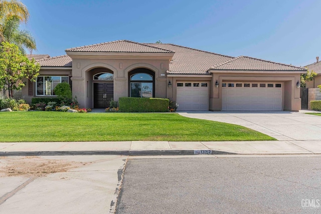 mediterranean / spanish-style home with stucco siding, driveway, a front lawn, and a garage