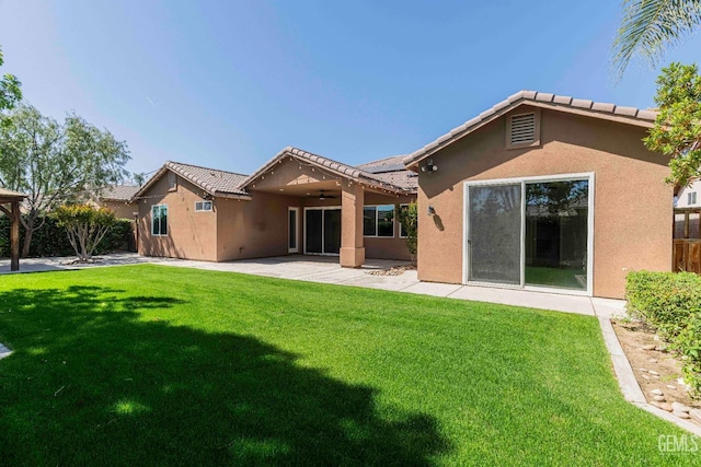 rear view of house featuring stucco siding, ceiling fan, a patio, a tile roof, and a lawn