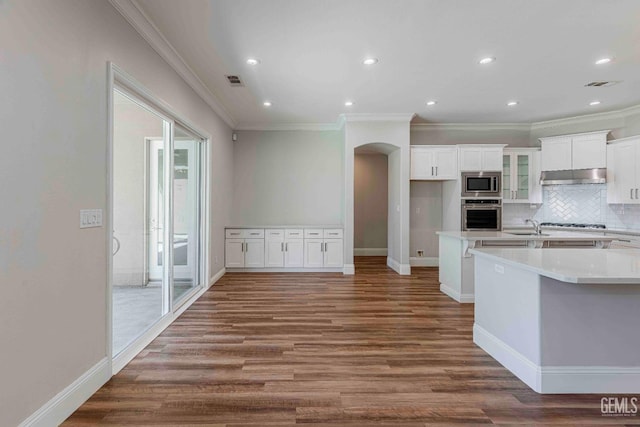 kitchen featuring arched walkways, stainless steel appliances, ornamental molding, a sink, and white cabinetry