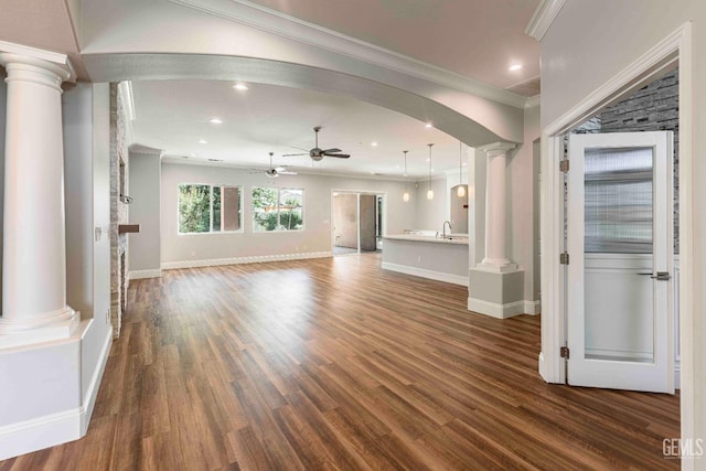 unfurnished living room featuring crown molding, a ceiling fan, decorative columns, and dark wood finished floors