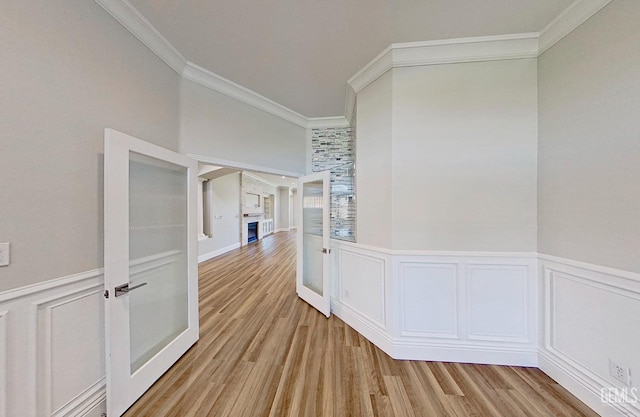 corridor with a decorative wall, light wood-type flooring, crown molding, and wainscoting