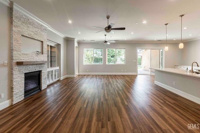 unfurnished living room with a sink, dark wood-type flooring, crown molding, a ceiling fan, and baseboards