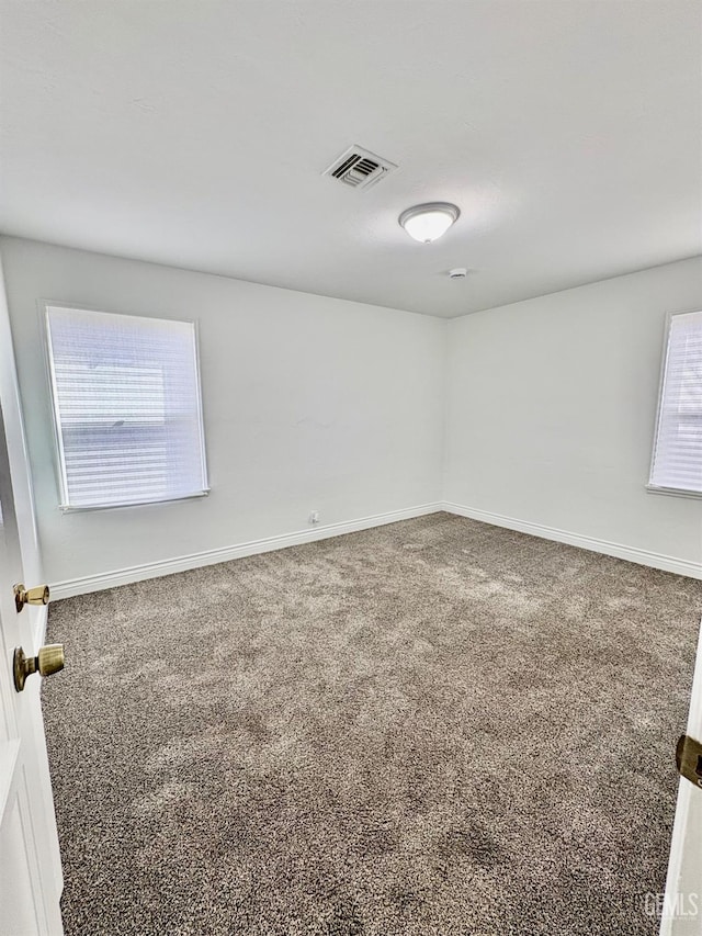 empty room with carpet, visible vents, and baseboards