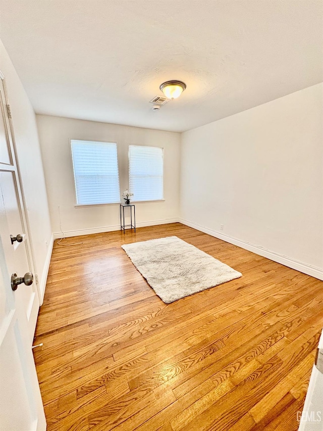 unfurnished room featuring baseboards, visible vents, and wood finished floors