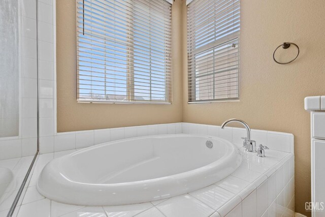 full bathroom with a bath, a textured wall, and a healthy amount of sunlight